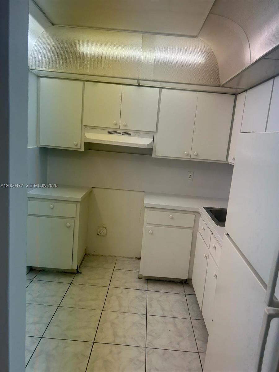 A small, white-cabinet kitchen features tiled flooring and a missing stove space — 15600 NW 7th Ave # 501, Miami FL 33169, MIAMI, FL