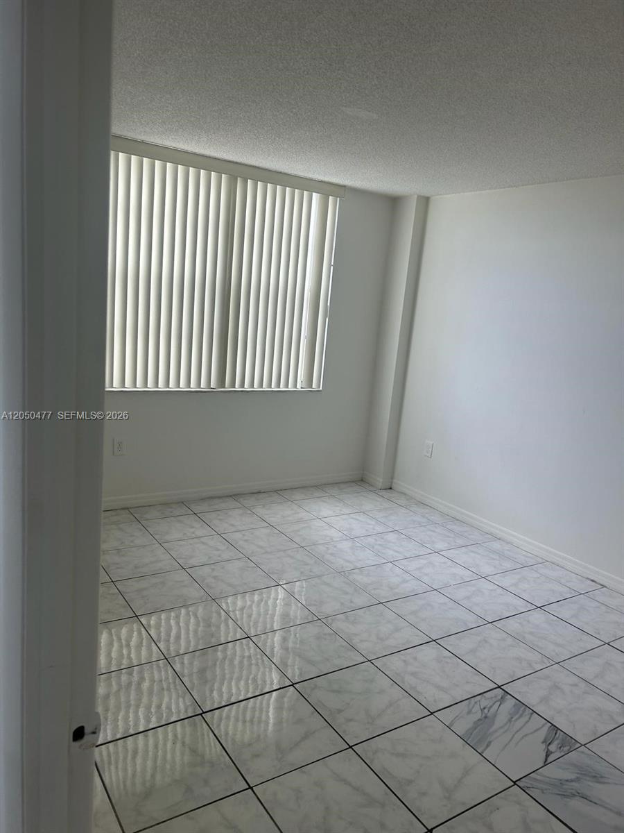 An empty room features white tiled floors, white walls, and a window with vertical blinds — 15600 NW 7th Ave # 501, Miami FL 33169, MIAMI, FL