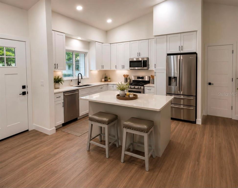 A modern kitchen features white cabinetry, stainless steel appliances, a central island, and wood-look flooring — 10722 WHISPERWOOD LANE, ORLANDO, FL
