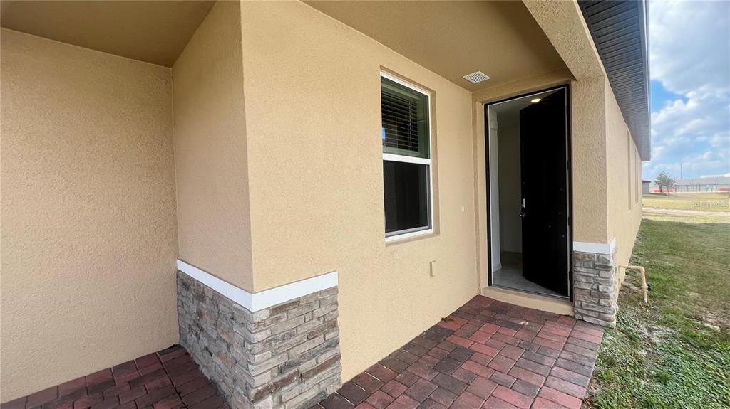 A tan stucco house exterior features a stone-accented corner, a brick patio, and an open door — 3185 VICEROY COURT, KISSIMMEE, FL