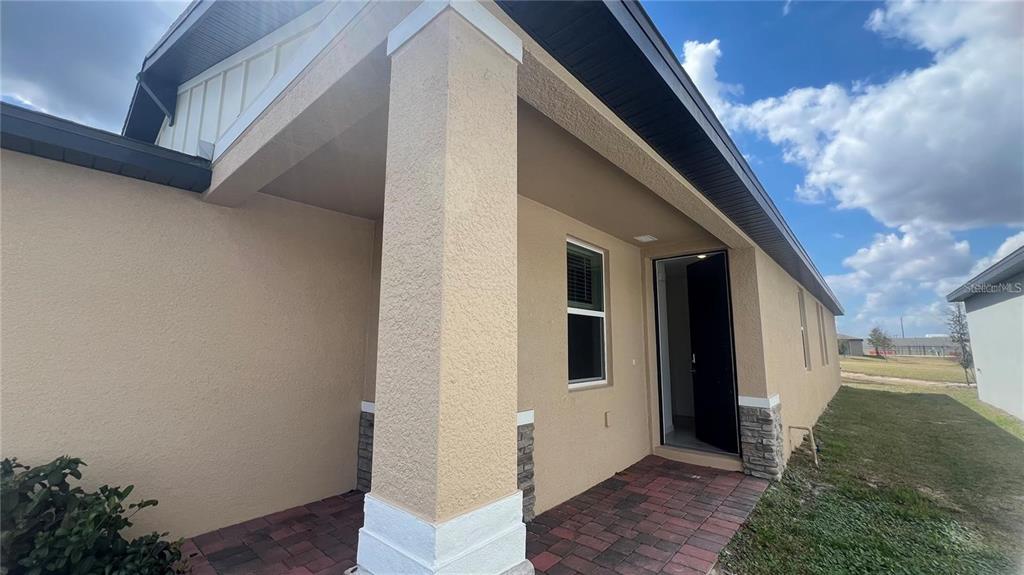 A covered entryway with a brick paver floor, tan stucco walls, and a stone-accented pillar — 3185 VICEROY COURT, KISSIMMEE, FL