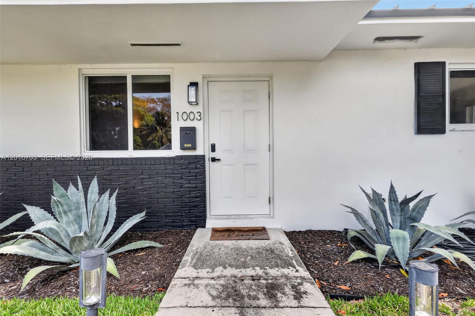 The exterior of a white house features a front door, a window, and two large agaves — 1003 NE 110th St # 1003, Biscayne Park FL 33161, BISCAYNE PARK, FL