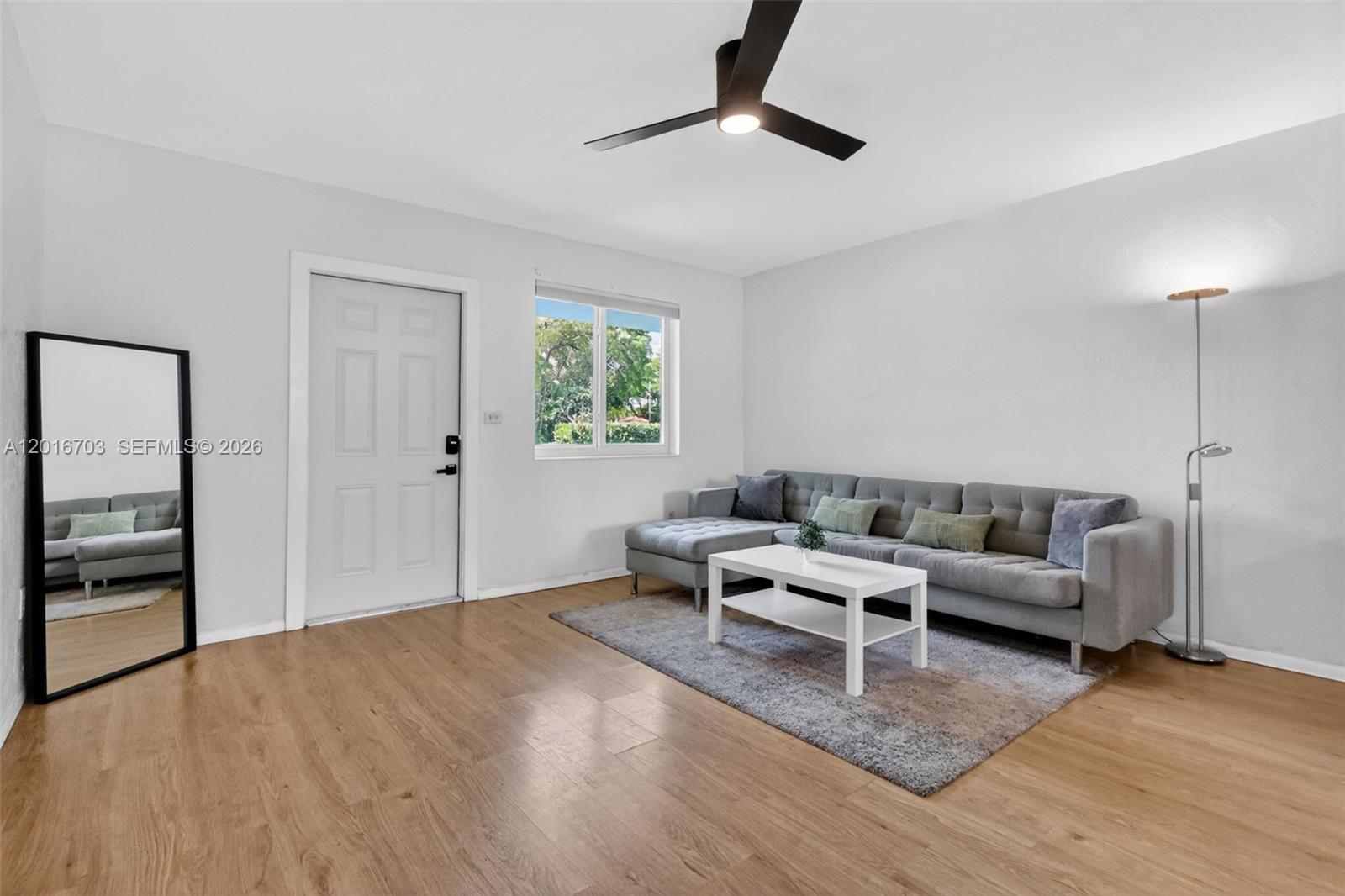 A living room features light wood flooring, a gray sectional sofa, and a ceiling fan — 1003 NE 110th St # 1003, Biscayne Park FL 33161, BISCAYNE PARK, FL