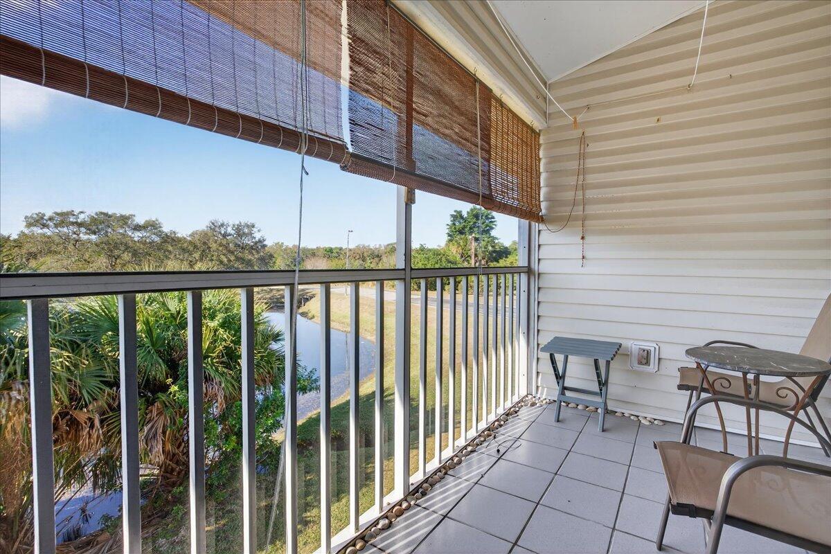 A screened-in balcony with tiled flooring, a small table, chairs, and a view of trees — 1810 Waterford Drive # 6, Vero Beach FL 32966, VERO BEACH, FL
