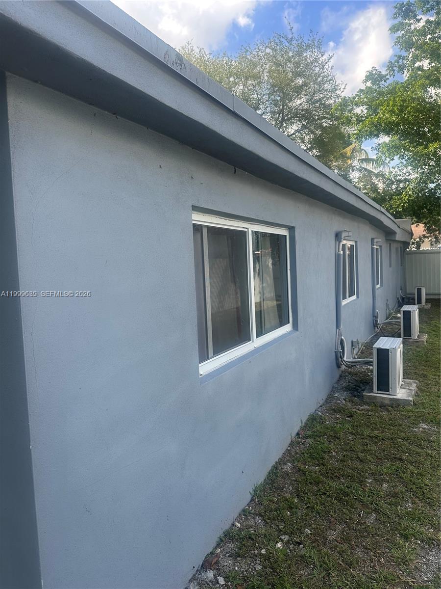 The exterior of a gray stucco house features two windows and multiple air conditioning units — 1790 NW 112th St, Miami FL 33167, MIAMI, FL