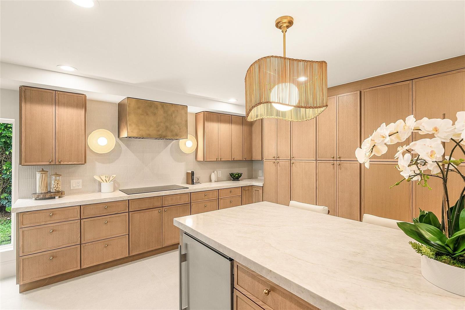 A modern kitchen features light wood cabinetry, a marble island, and a gold range hood — 4877 Pineview Circle, Delray Beach FL 33445, DELRAY BEACH, FL