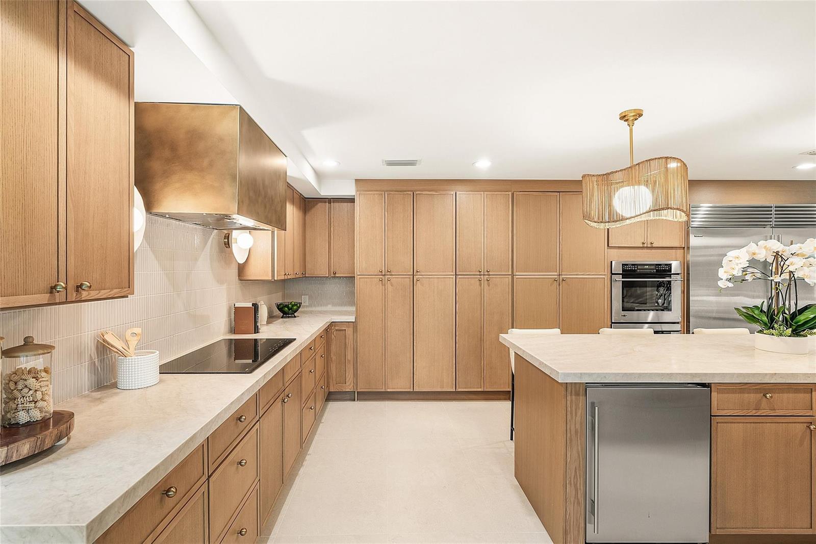 A modern kitchen features light wood cabinetry, a stone island, and a brass range hood — 4877 Pineview Circle, Delray Beach FL 33445, DELRAY BEACH, FL