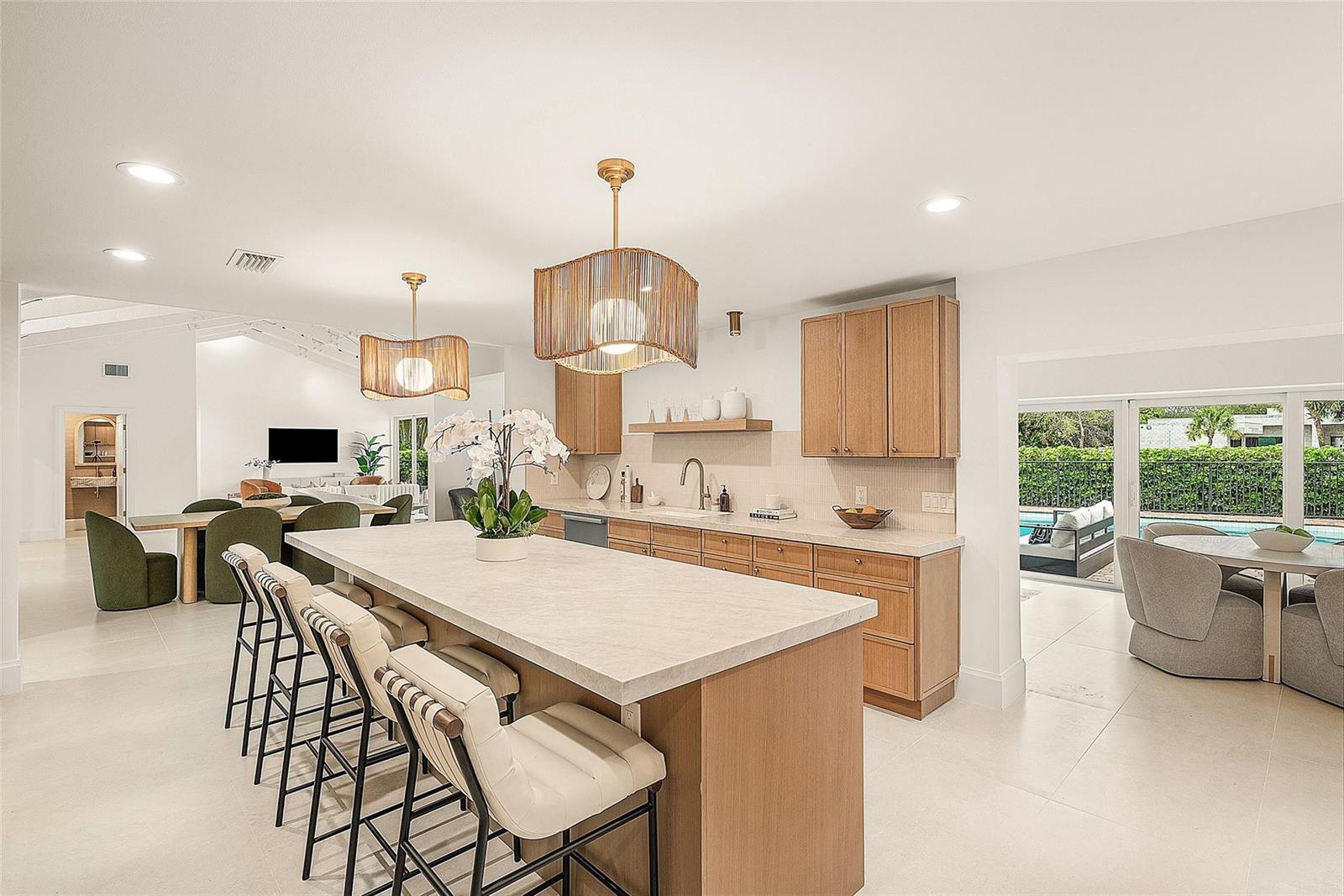 A modern kitchen features a large island with bar seating, light wood cabinetry, and pendant lighting — 4877 Pineview Circle, Delray Beach FL 33445, DELRAY BEACH, FL