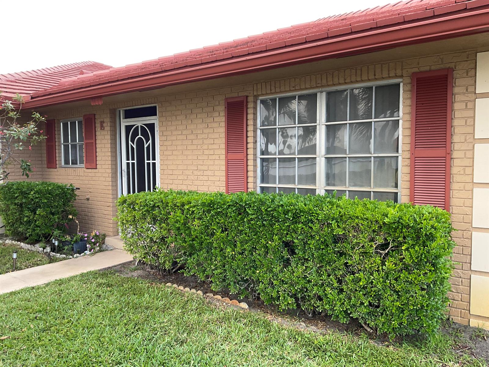 A tan brick house features a red roof, red shutters, and a green hedge — 1473 SW 27th Avenue # 1e, Boynton Beach FL 33426, BOYNTON BEACH, FL