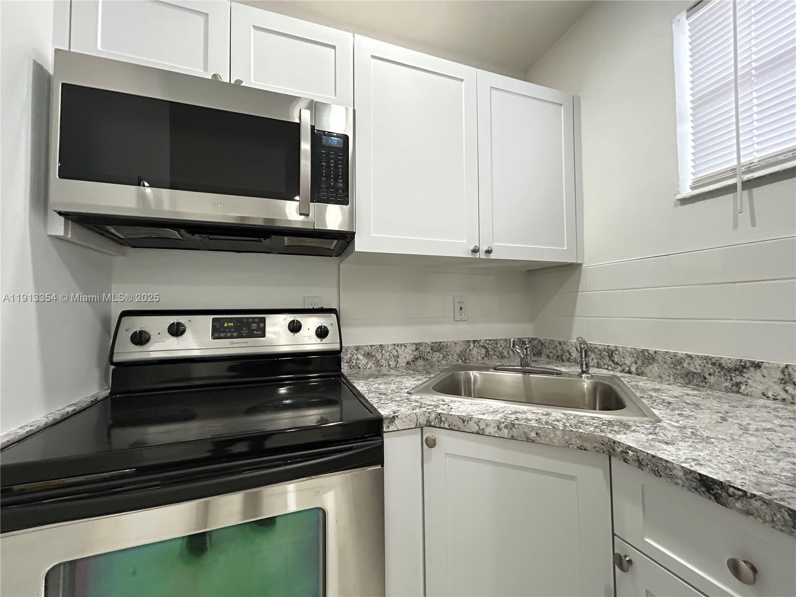 A kitchen features white cabinets, stainless steel appliances, and a corner sink with granite countertops — 6950 NW 8th Ave # 3, Miami FL 33150, MIAMI, FL