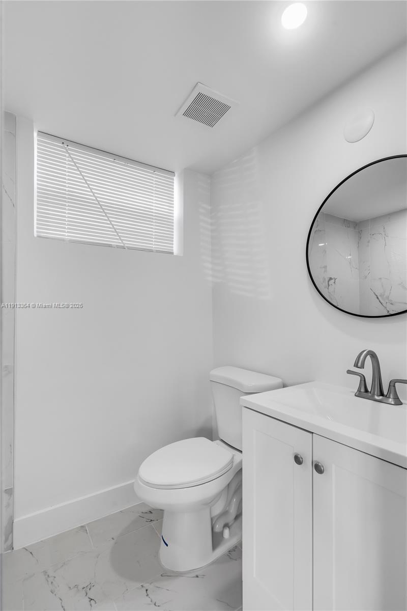 A modern bathroom features a white vanity, a round mirror, and a toilet — 6950 NW 8th Ave # 3, Miami FL 33150, MIAMI, FL