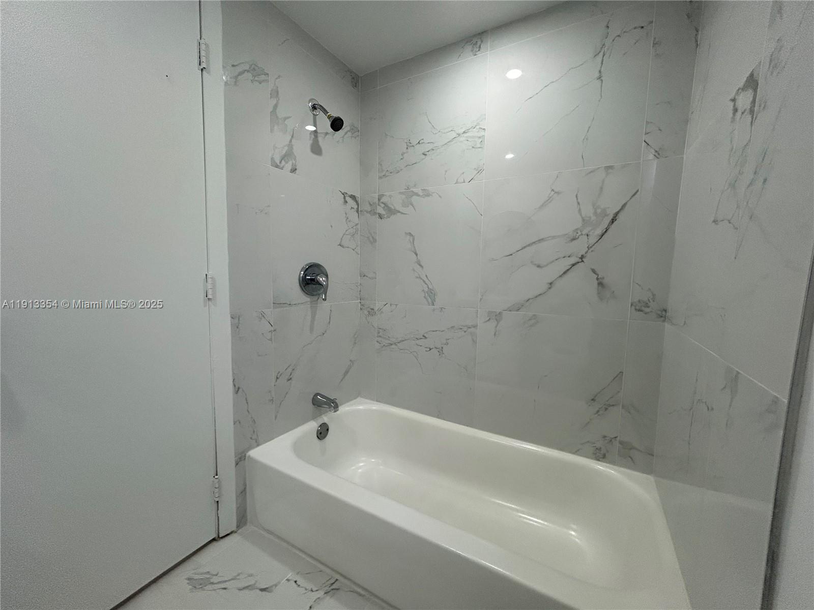 A white bathtub is installed against walls covered in large, white marble-patterned tiles — 6950 NW 8th Ave # 3, Miami FL 33150, MIAMI, FL