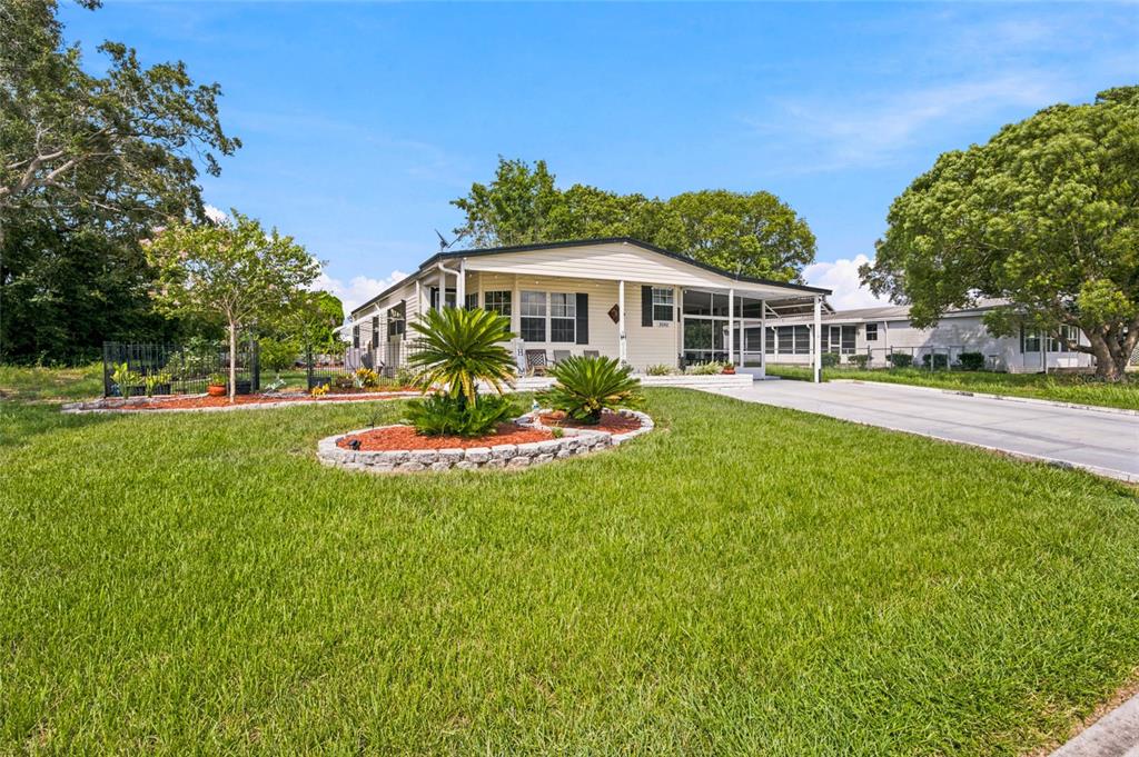 A single-story manufactured home features a front porch, a concrete driveway, and landscaped garden beds — 9242 DENMARSH DRIVE, BROOKSVILLE, FL