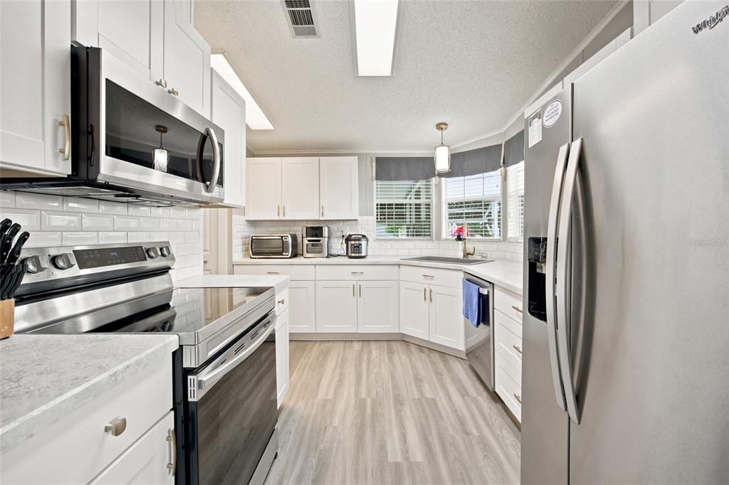 A bright kitchen features white cabinets, stainless steel appliances, a subway tile backsplash, and wood-look flooring — 9242 DENMARSH DRIVE, BROOKSVILLE, FL
