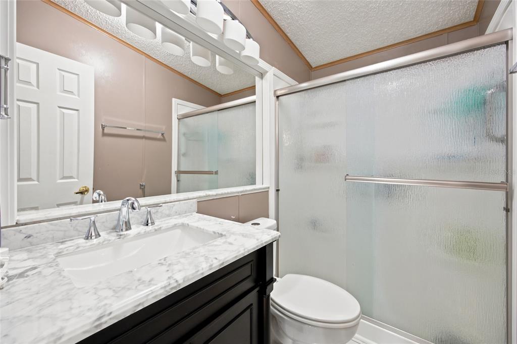 A bathroom features a black vanity with a marble countertop, a toilet, and a shower — 9242 DENMARSH DRIVE, BROOKSVILLE, FL