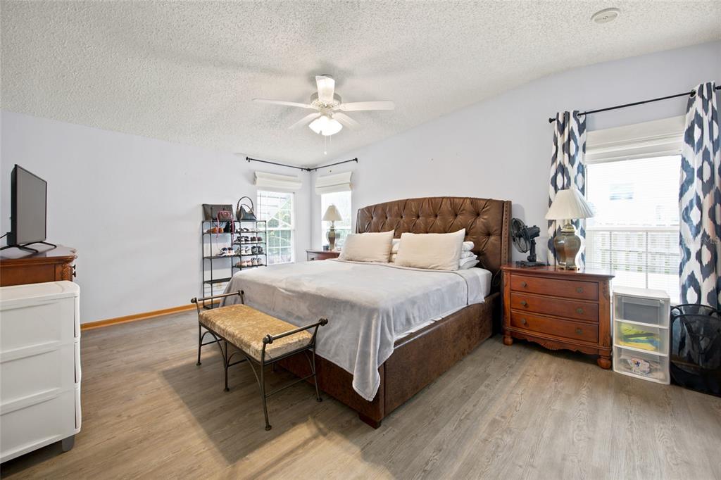 A bedroom features a tufted leather bed, wood-look flooring, and a ceiling fan — 9242 DENMARSH DRIVE, BROOKSVILLE, FL