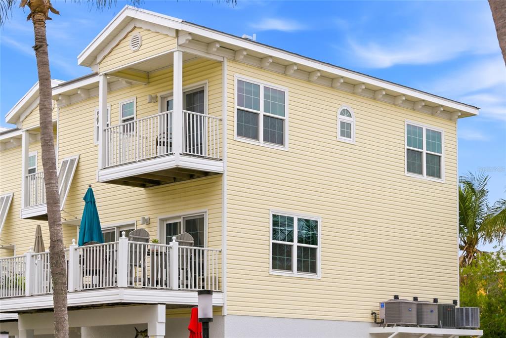 A yellow-sided, multi-story house features a balcony, a deck, and several windows — 1473 GULF DRIVE N, BRADENTON BEACH, FL