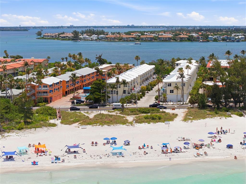 An aerial view shows beachgoers on white sand in front of multi-story residential buildings — 1473 GULF DRIVE N, BRADENTON BEACH, FL