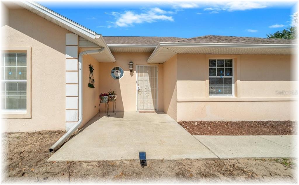 The exterior of a peach-colored house features a concrete porch, a security door, and windows — 8740 SE 61 AVENUE, OCALA, FL