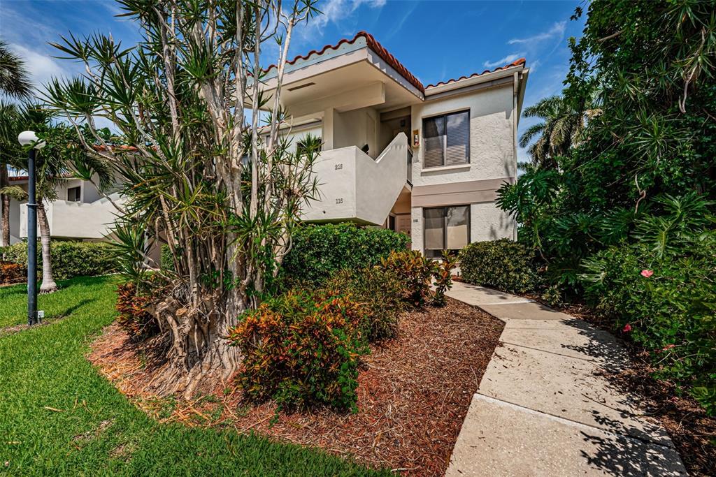 A two-story stucco apartment building features a tiled roof, exterior stairs, and lush landscaping — 6273 BAHIA DEL MAR BOULEVARD UNIT 116, ST PETERSBURG, FL