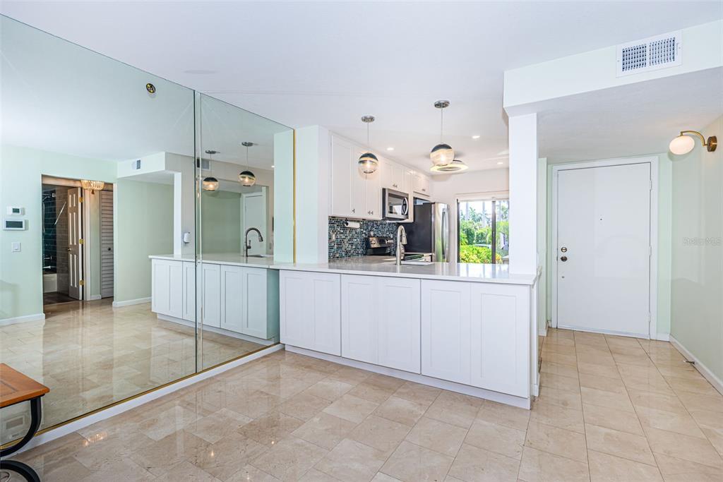 A kitchen with white cabinets, a tiled backsplash, and a mirrored wall in an open space — 6273 BAHIA DEL MAR BOULEVARD UNIT 116, ST PETERSBURG, FL