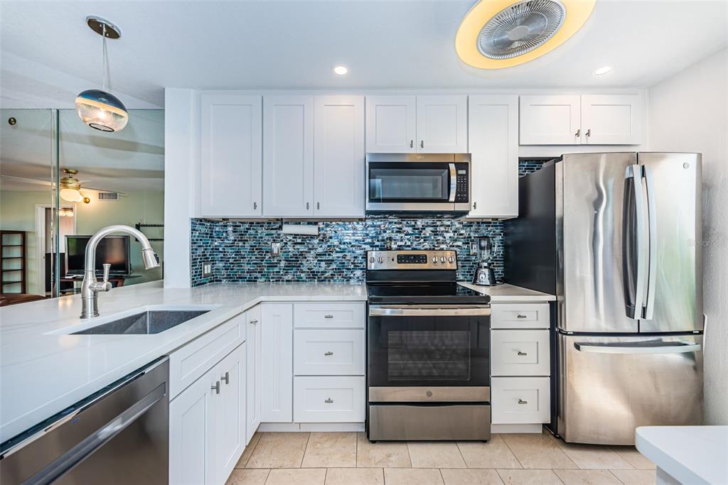 A kitchen features white cabinets, stainless steel appliances, and a blue mosaic tile backsplash — 6273 BAHIA DEL MAR BOULEVARD UNIT 116, ST PETERSBURG, FL