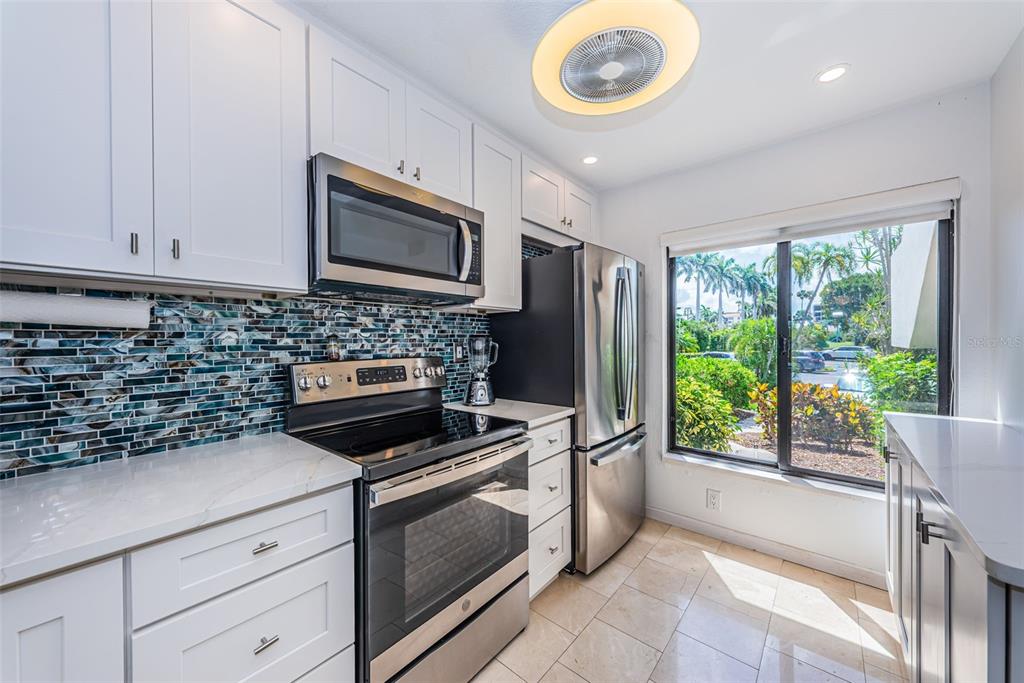 A kitchen features white cabinets, stainless steel appliances, a blue mosaic backsplash, and a window — 6273 BAHIA DEL MAR BOULEVARD UNIT 116, ST PETERSBURG, FL