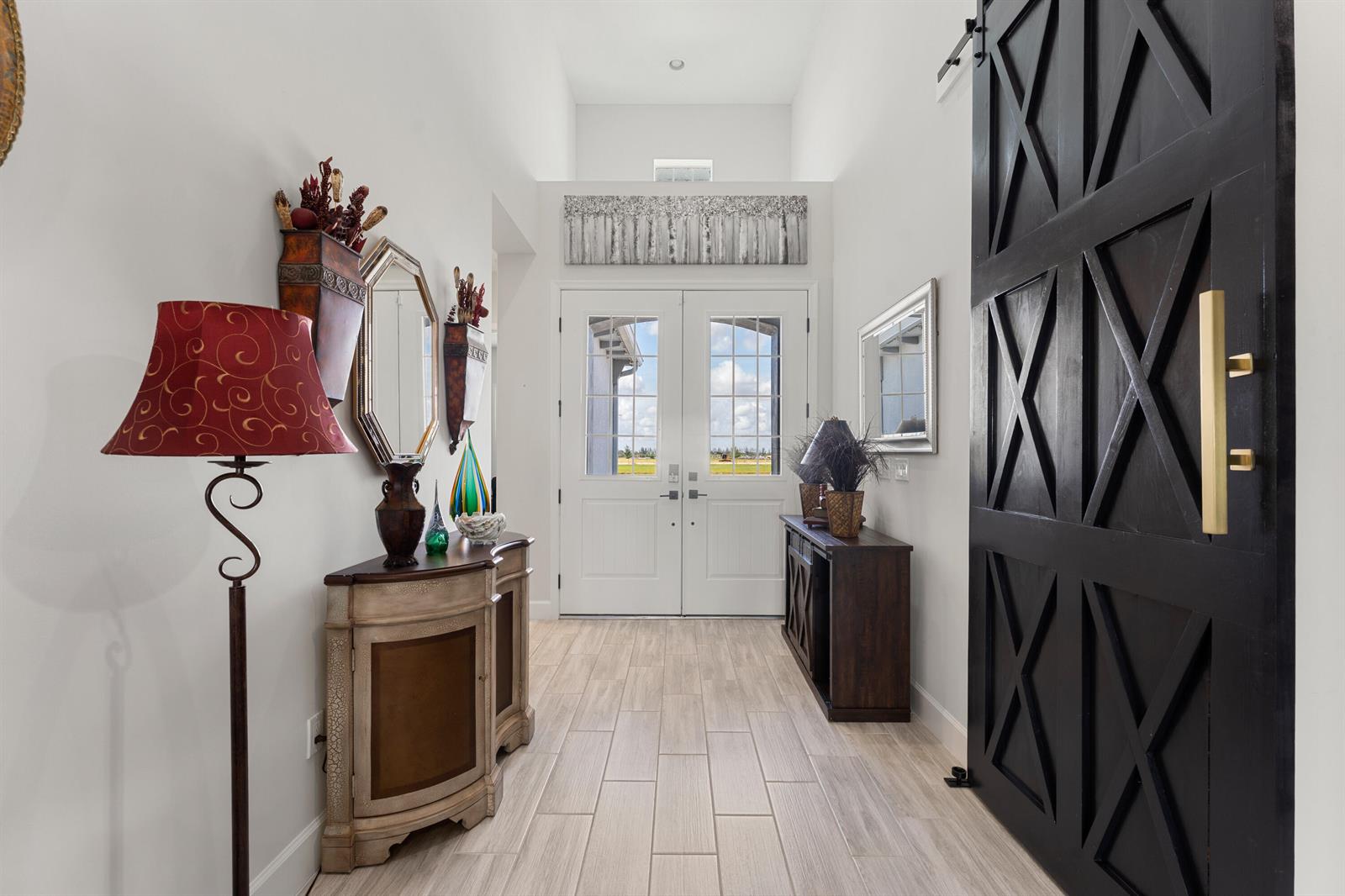 A bright entryway features a black barn door, double glass front doors, and tiled flooring — 13530 Spruce Pine Drive, FL 33470, FL