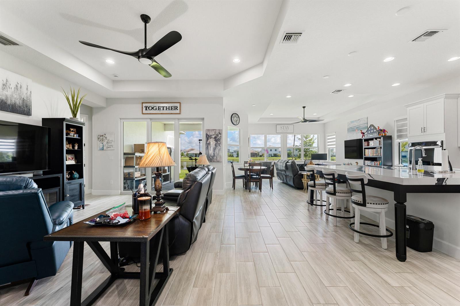 An open-concept living room and kitchen feature light tile flooring, white cabinetry, and large windows — 13530 Spruce Pine Drive, FL 33470, FL