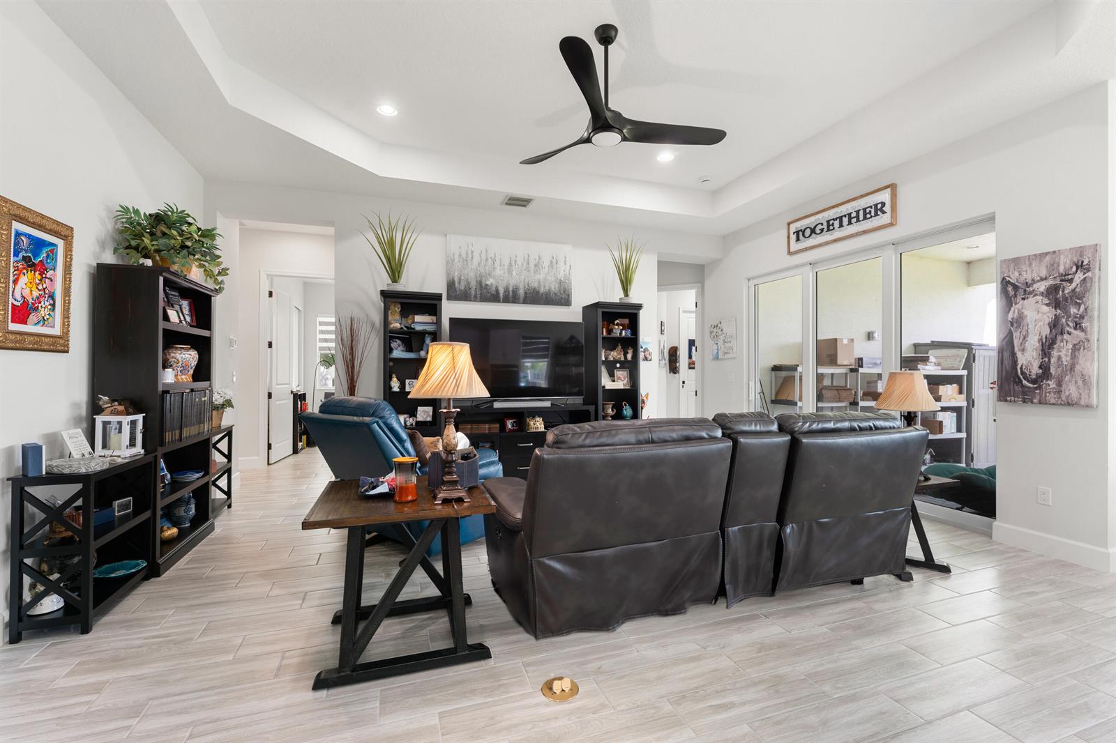 A living room features a dark leather sofa, a television, shelving units, and a ceiling fan — 13530 Spruce Pine Drive, FL 33470, FL