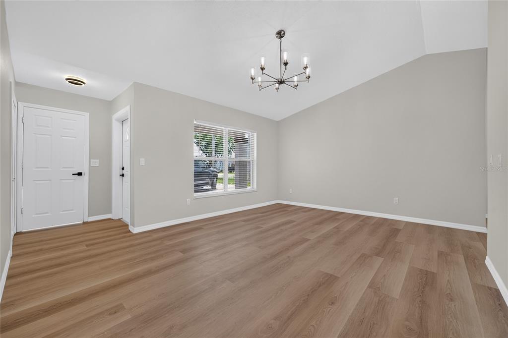 An empty room with light gray walls, wood-look flooring, and a vaulted ceiling with chandelier — 631 STANFORD DRIVE, ALTAMONTE SPRINGS, FL