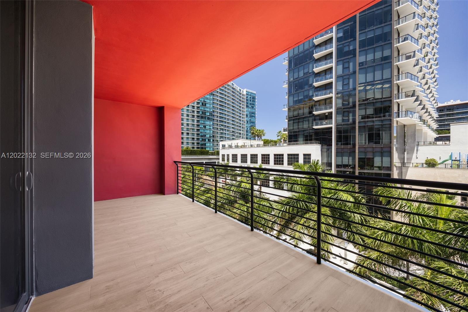 A balcony features light wood-look flooring, a bright red ceiling, and a black metal railing — 90 NE 32nd St # 504, Miami FL 33127, MIAMI, FL