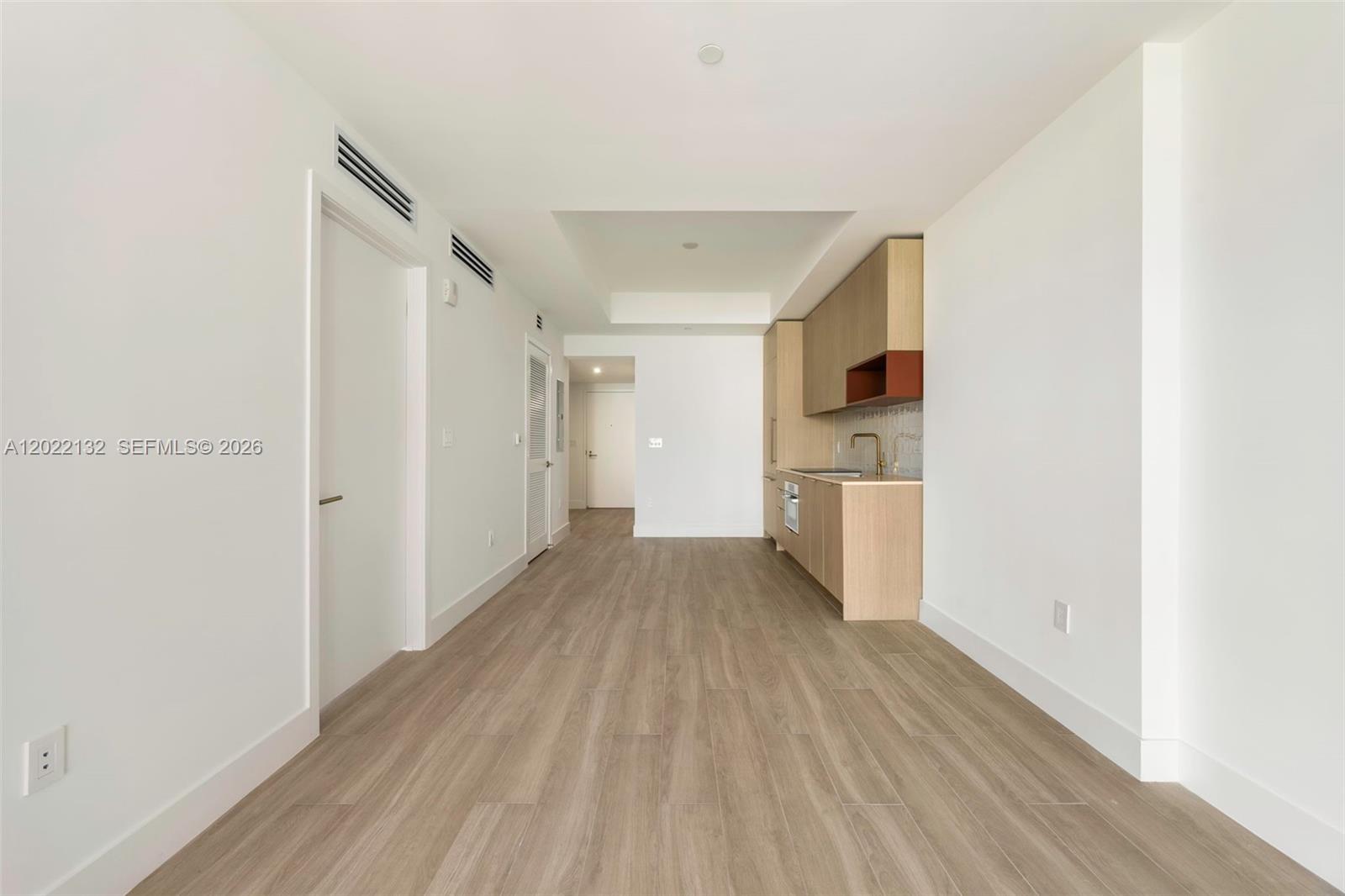 A minimalist kitchen area features light wood cabinetry, white walls, and wood-look flooring — 90 NE 32nd St # 504, Miami FL 33127, MIAMI, FL
