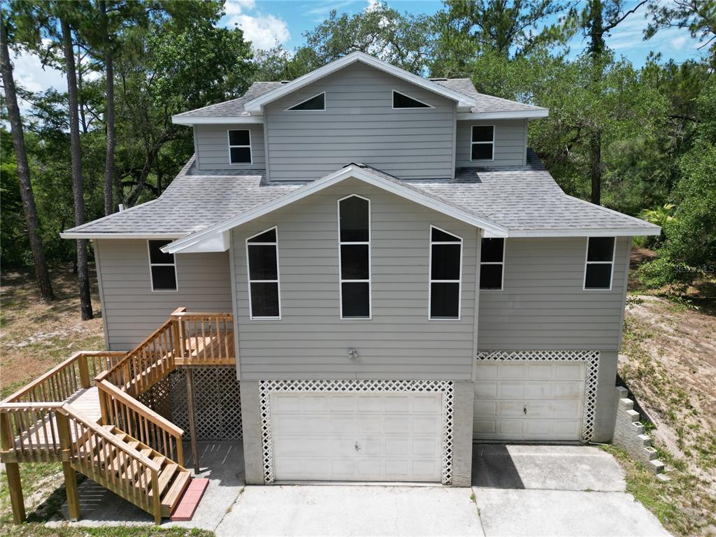 A two-story house with gray siding, a wooden staircase, and two ground-level garage doors — 3451 MCKETHAN ROAD, DADE CITY, FL