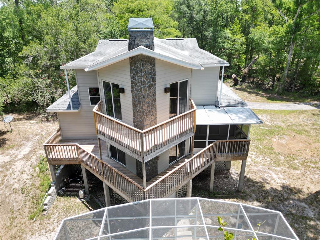 An elevated house with a stone chimney, wrap-around wooden decks, and a screened pool enclosure — 3451 MCKETHAN ROAD, DADE CITY, FL