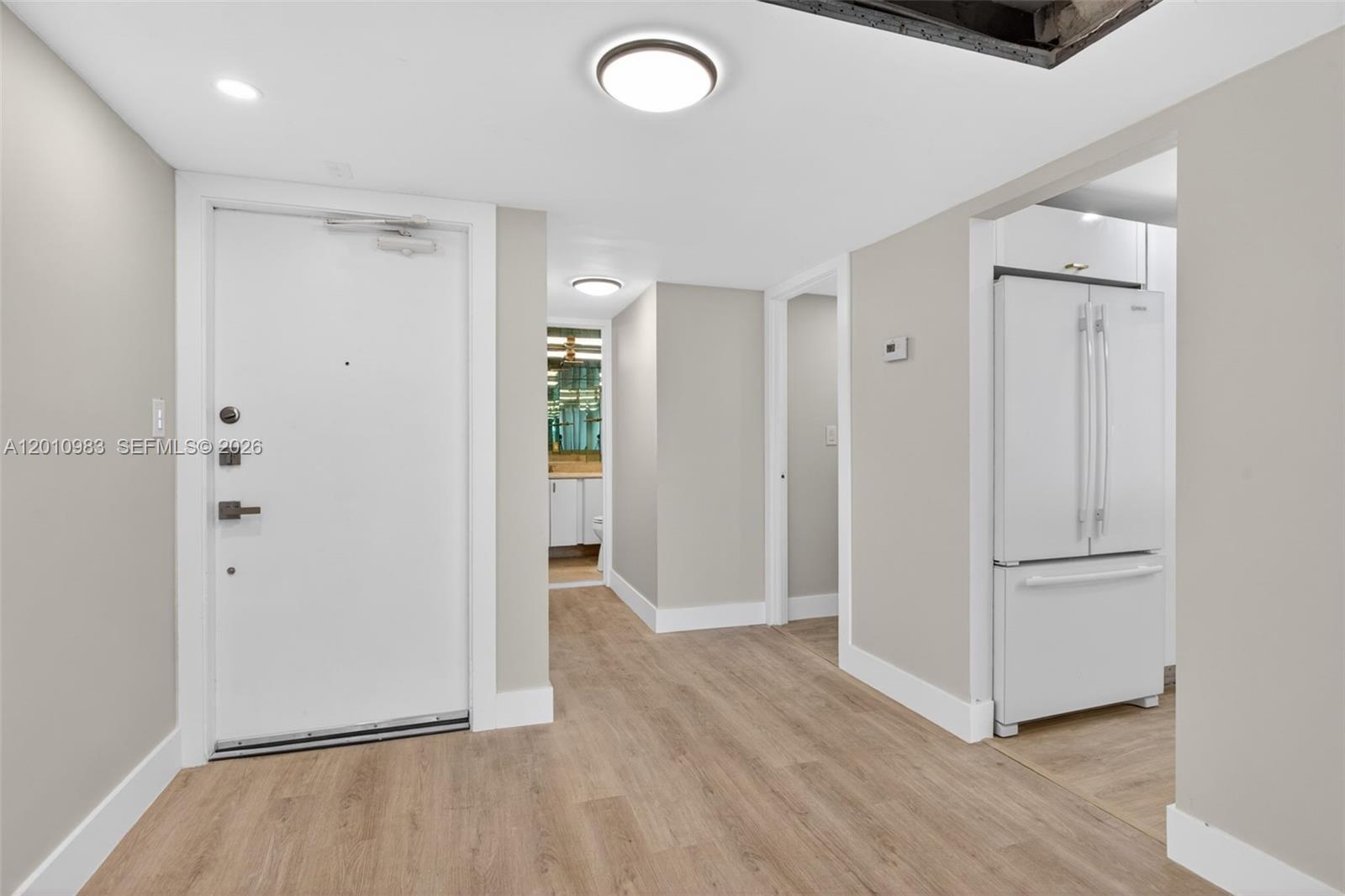 An entryway with light wood flooring leads to a hallway, a bathroom, and a kitchen — 3090 N Course Dr # 807, Pompano Beach FL 33069, POMPANO BEACH, FL