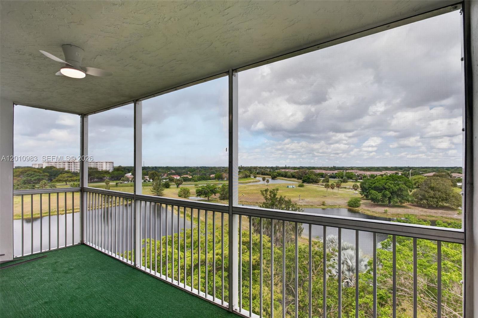 A screened-in balcony features green carpeting, a ceiling fan, and a view of a lake — 3090 N Course Dr # 807, Pompano Beach FL 33069, POMPANO BEACH, FL