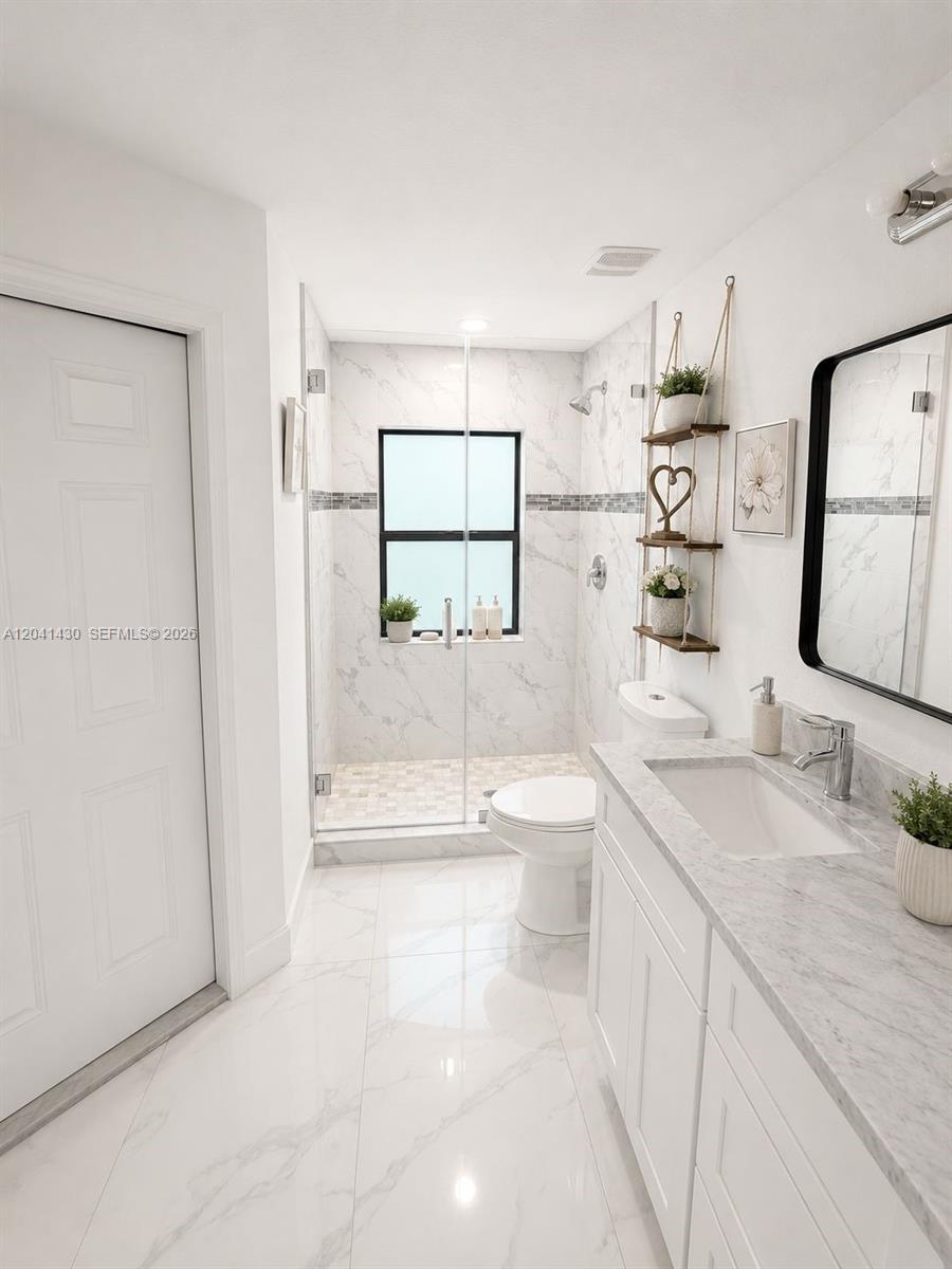 A modern bathroom features a glass-enclosed shower, marble-look tile, and a white vanity — 1006 Rush Ave, Lehigh Acres FL 33972, LEHIGH ACRES, FL