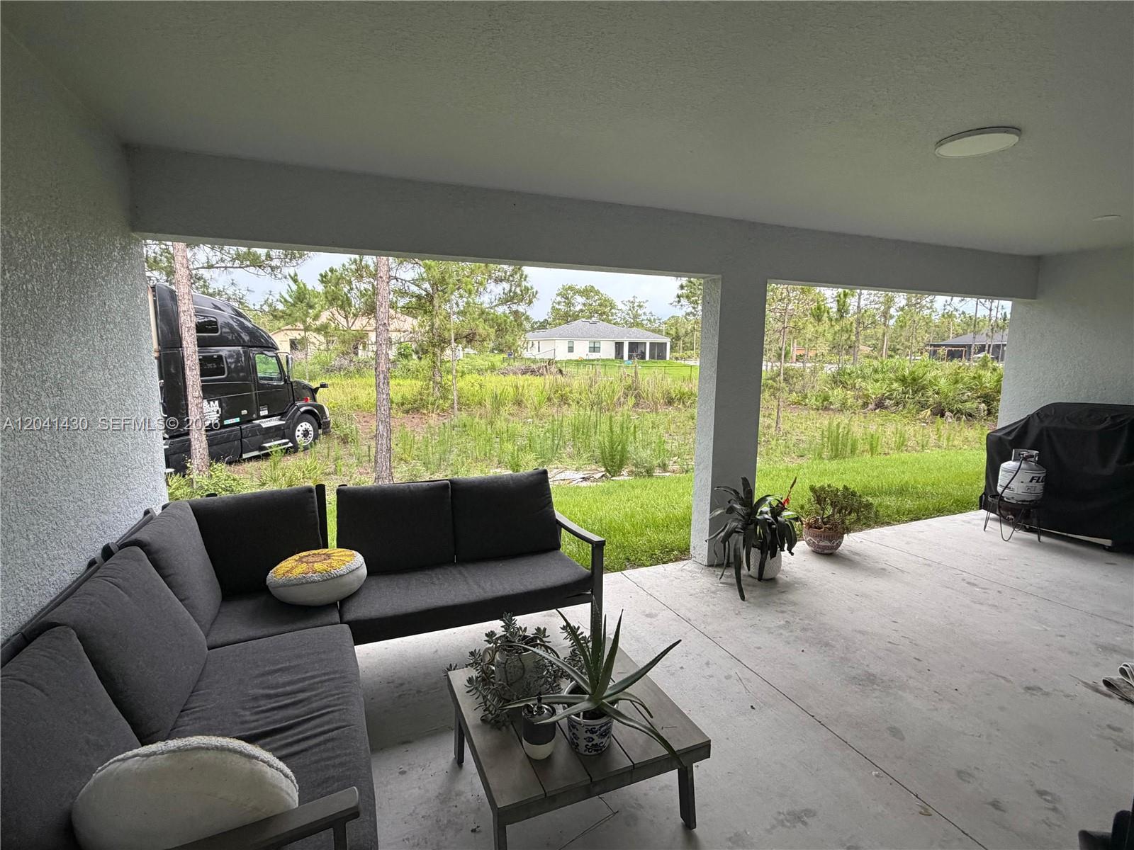 A covered patio features a sectional sofa, a small table, and a view of a yard — 1006 Rush Ave, Lehigh Acres FL 33972, LEHIGH ACRES, FL