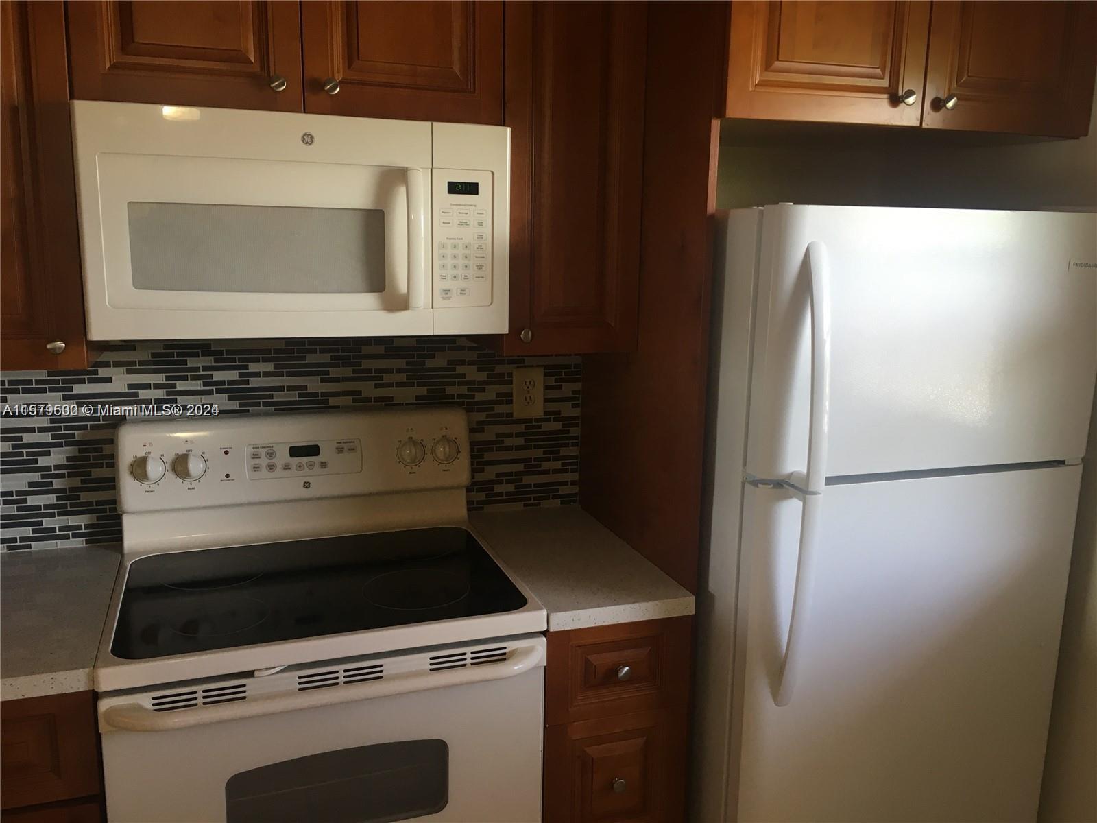 A kitchen features wood cabinets, white appliances, and a dark tiled backsplash — 3396 Foxcroft Rd # 308, Miramar FL 33025, MIRAMAR, FL
