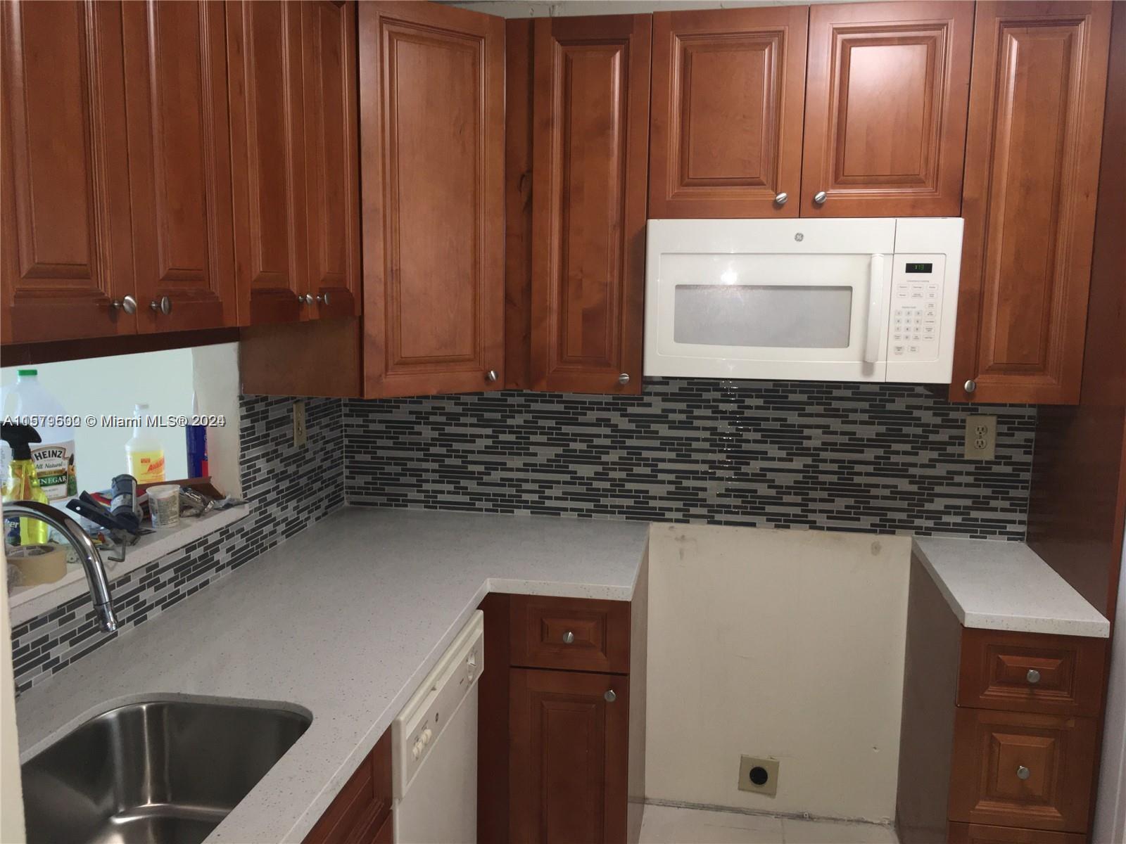 A kitchen features wood cabinets, a white microwave, a gray countertop, and a tiled backsplash — 3396 Foxcroft Rd # 308, Miramar FL 33025, MIRAMAR, FL