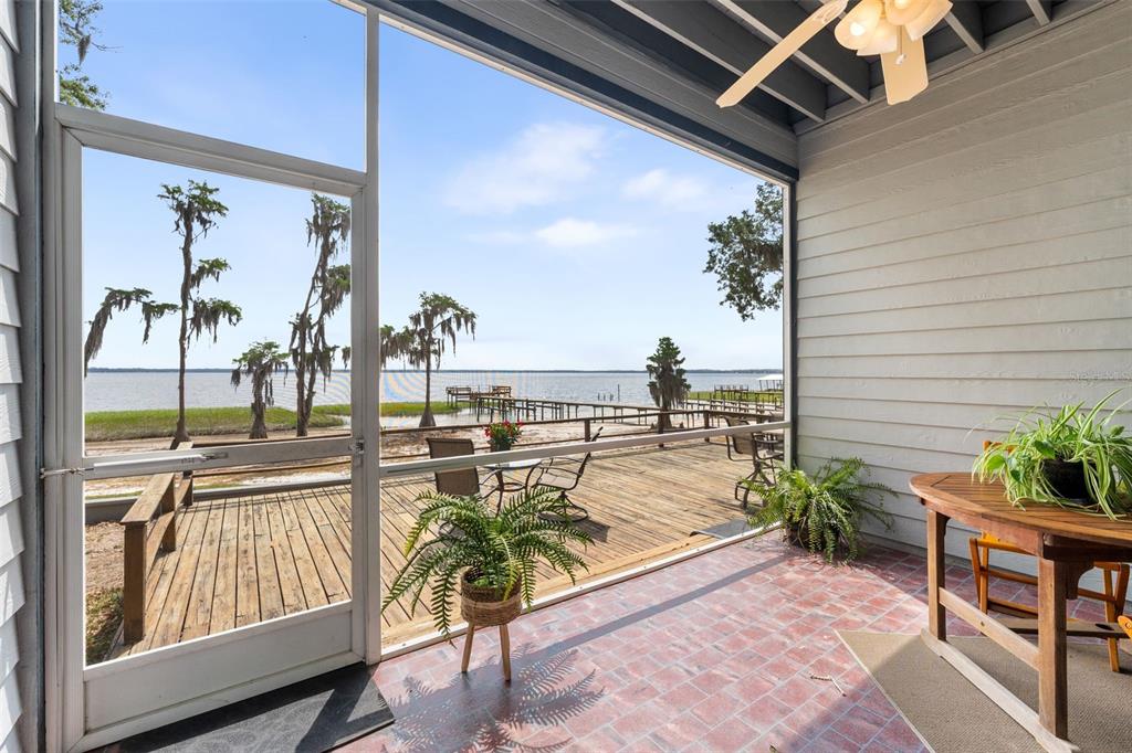 A screened-in porch with a tiled floor overlooks a wooden deck and a lake — 21134 NE 101ST AVENUE, EARLETON, FL