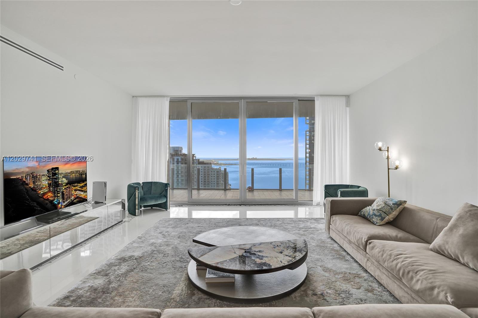 A modern living room features a beige sofa, a tiered coffee table, and floor-to-ceiling windows — 300 Biscayne Boulevard Way # 3304C, Miami FL 33131, MIAMI, FL