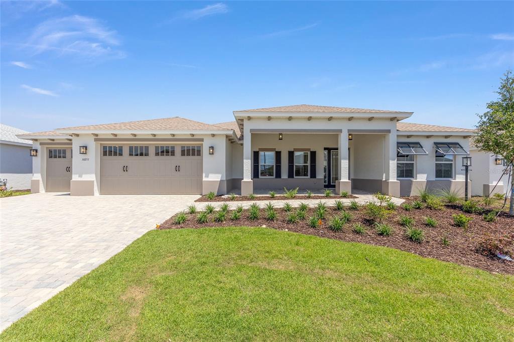A single-story house with a beige stucco exterior, a three-car garage, and a covered porch — 10211 SW 82ND PL ROAD, OCALA, FL