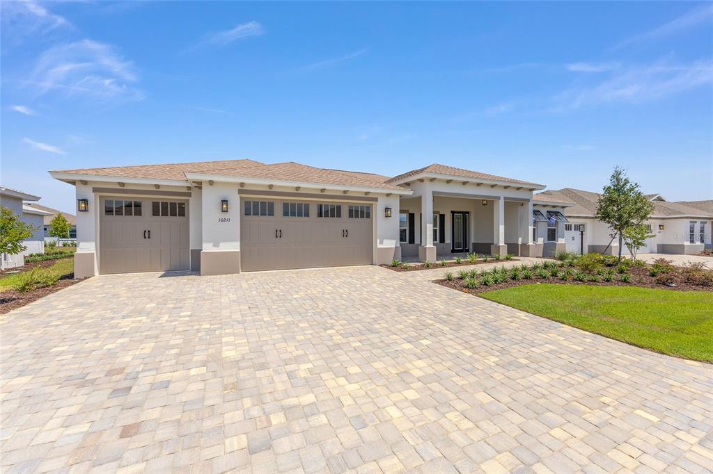 A single-story house with a three-car garage and a paved driveway under a blue sky — 10211 SW 82ND PL ROAD, OCALA, FL