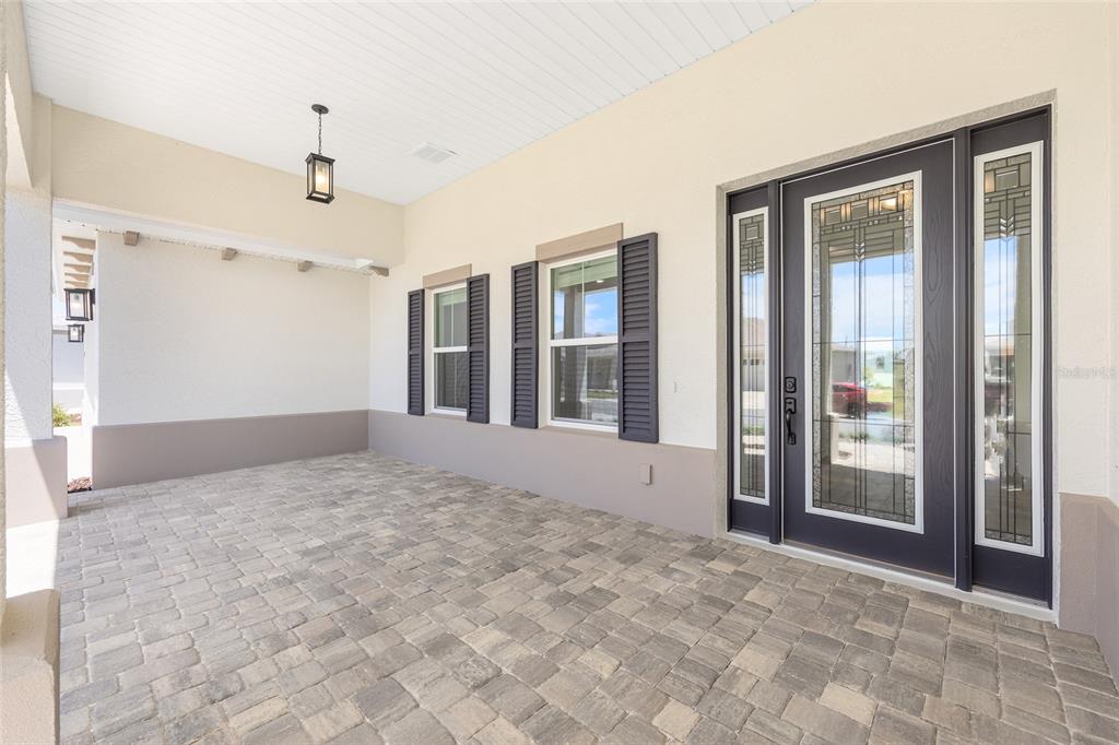 A covered entryway features a paver floor, a dark front door with sidelights, and shutters — 10211 SW 82ND PL ROAD, OCALA, FL
