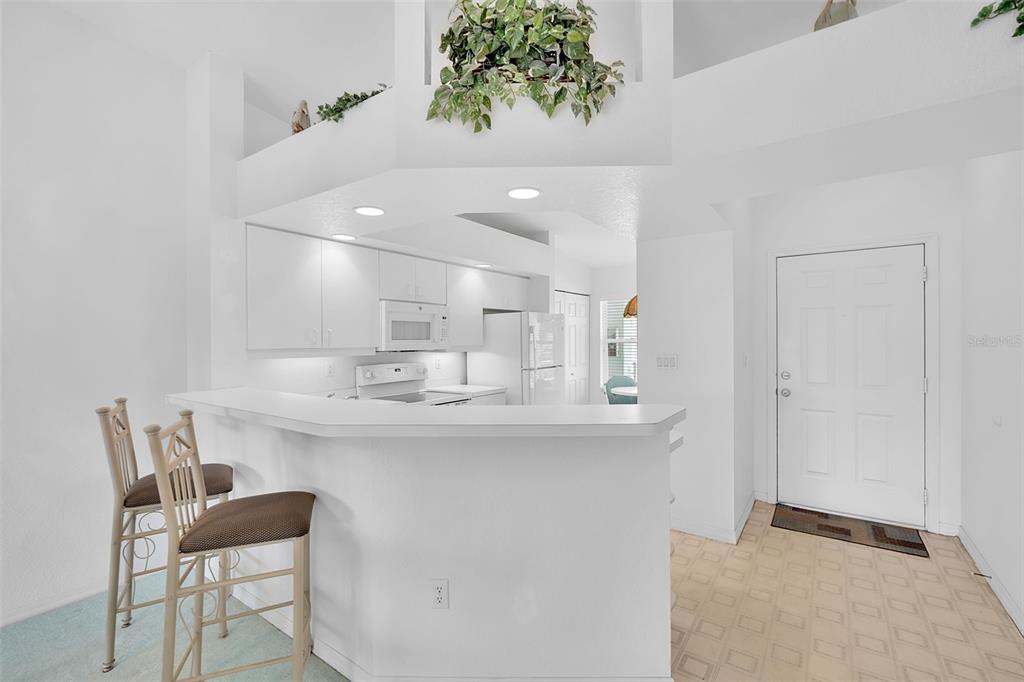 A white kitchen with a breakfast bar, two stools, and an adjacent entryway door — 5725 GREENWOOD AVENUE UNIT 4201, NORTH PORT, FL