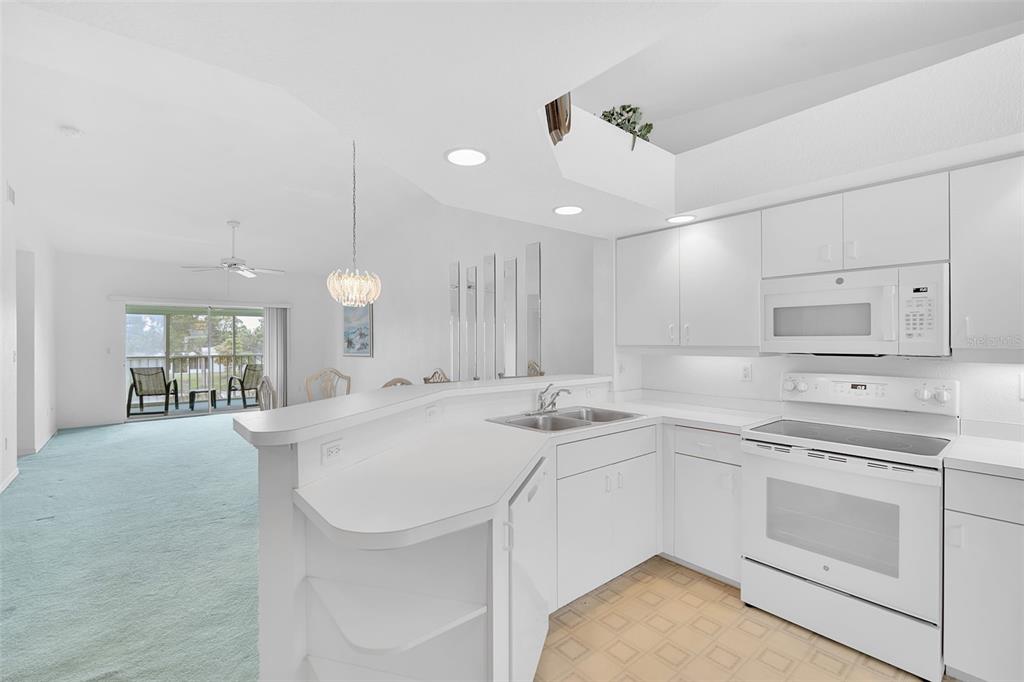 A white kitchen with a breakfast bar overlooks a living area with light blue carpeting — 5725 GREENWOOD AVENUE UNIT 4201, NORTH PORT, FL