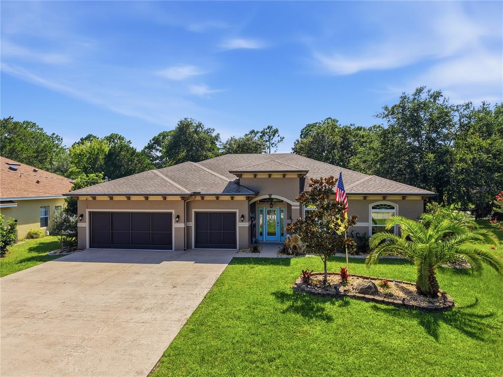 A single-story house with a three-car garage, a blue front door, and a landscaped yard — 225 BIRCHWOOD DRIVE, PALM COAST, FL