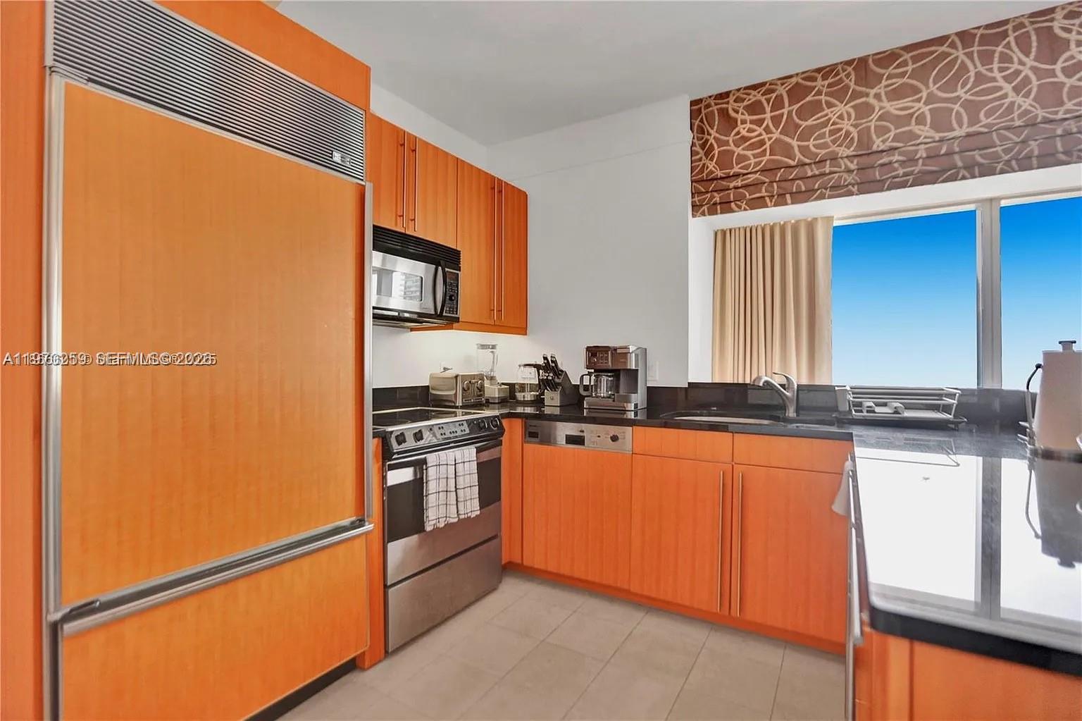 A kitchen features orange wood cabinetry, black countertops, and stainless steel appliances — 1435 Brickell Ave # 3212, Miami FL 33131, MIAMI, FL